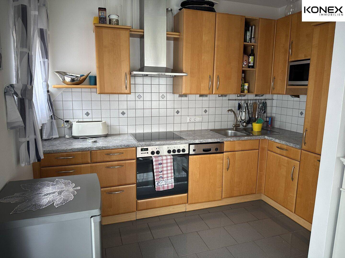 Funktionale Einbauküche mit Holzschränken, Elektrogeräten und gefliestem Spritzschutz.