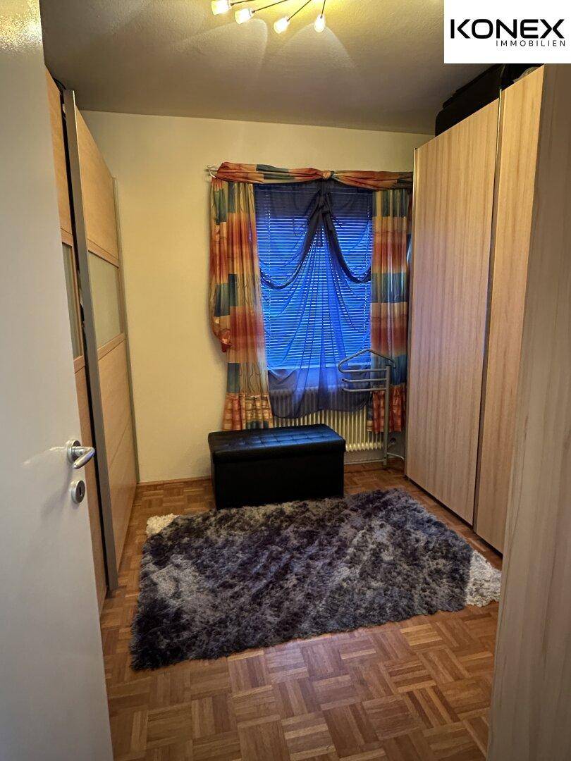 Kleines Schlafzimmer mit Einbauschränken, Teppich und farbigen Vorhängen.