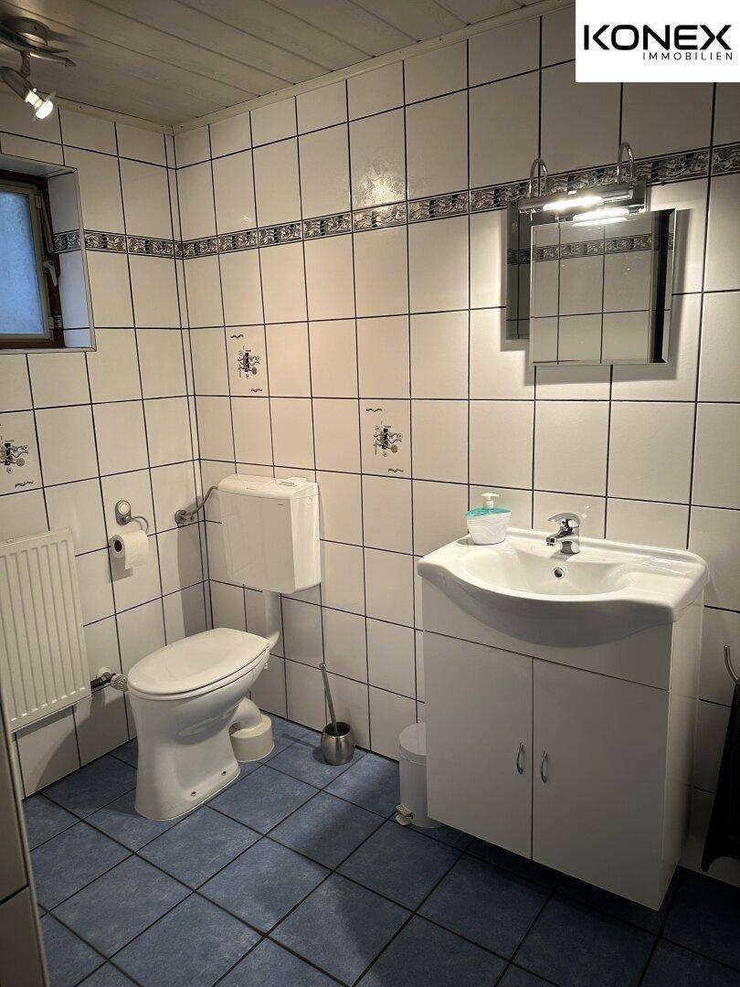 Badezimmer mit WC, Waschbecken, Spiegel und blauen Bodenfliesen.