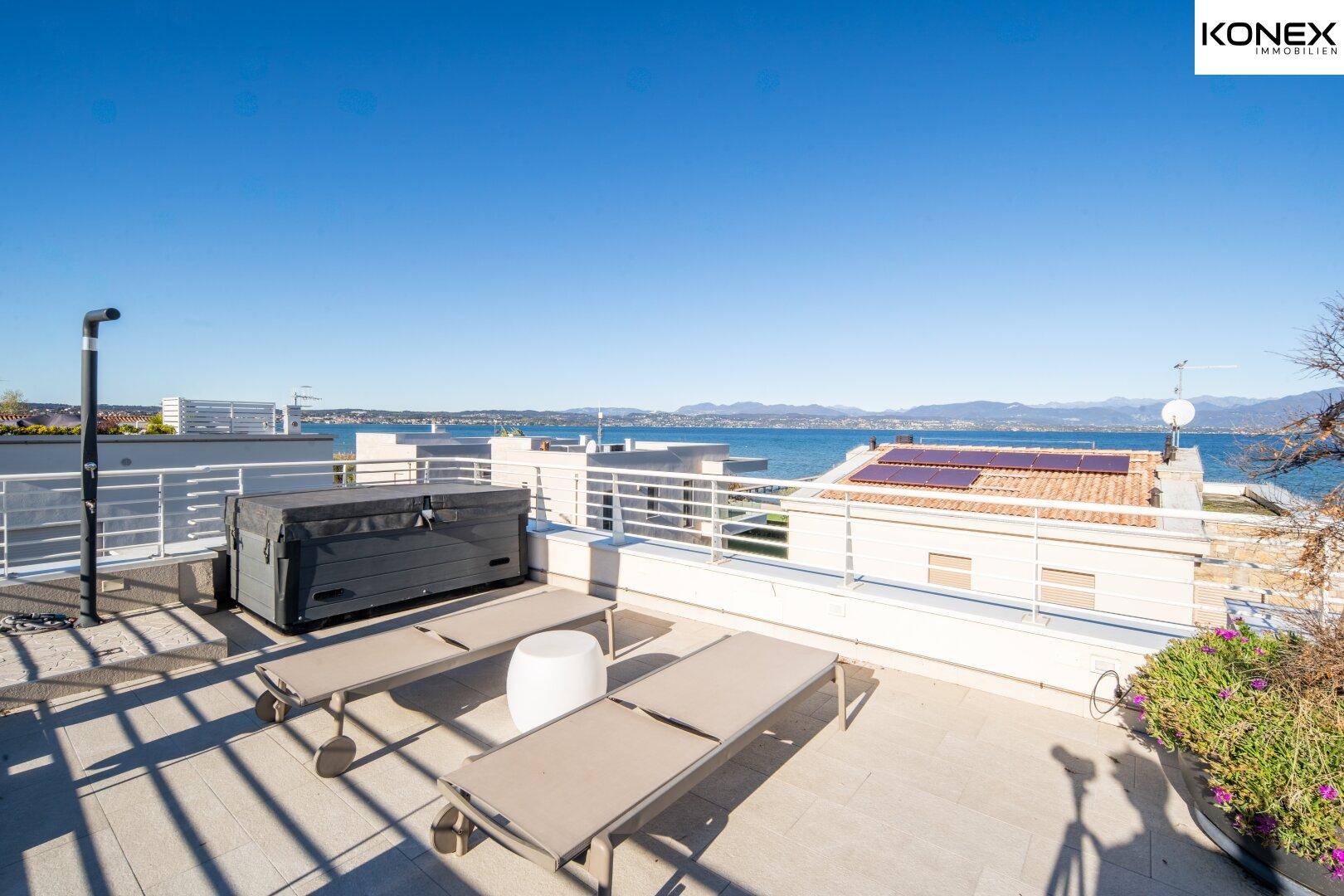 Große Dachterrasse mit Whirlpool, Sonnenliegen und Panoramablick auf den See.