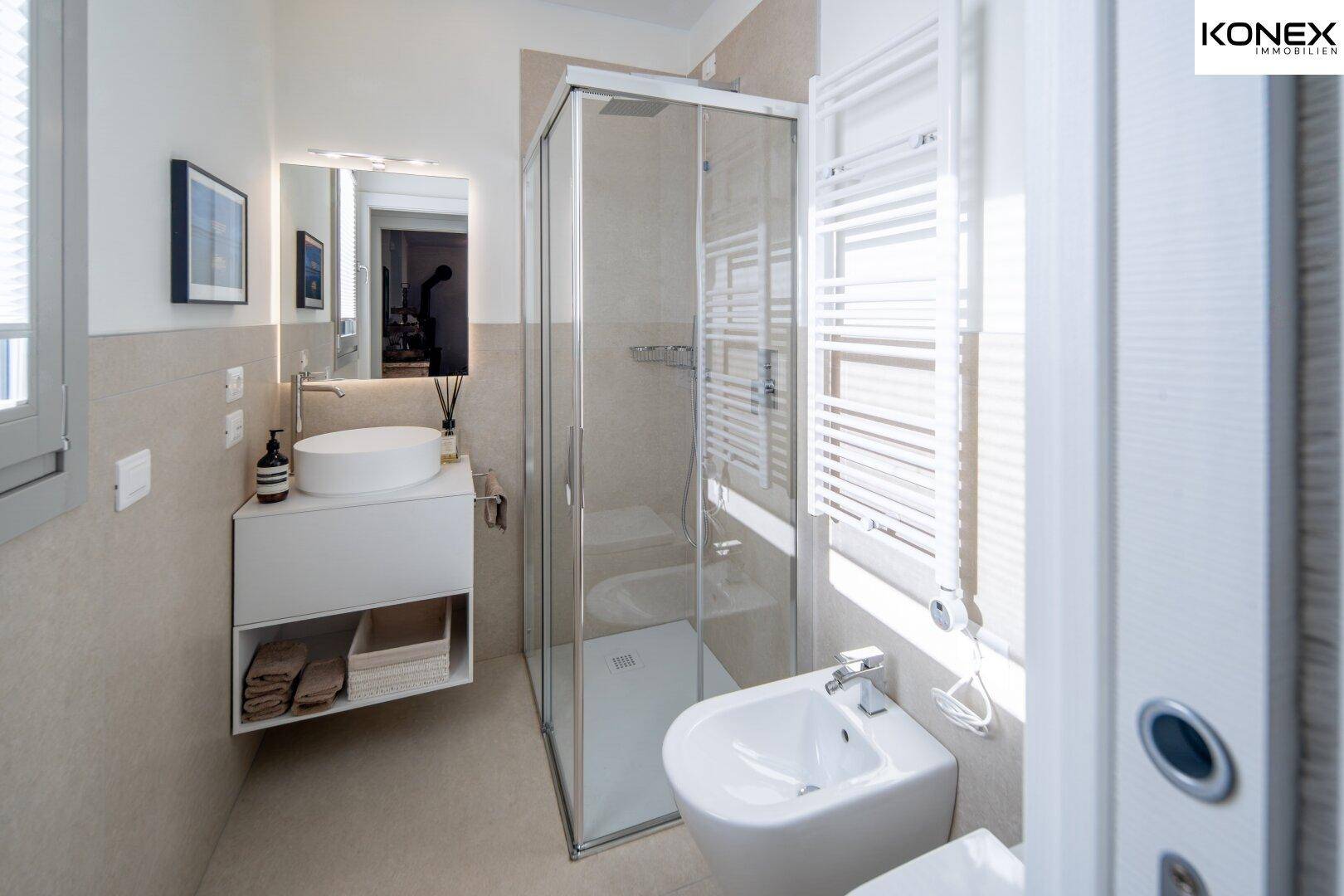 Modernes Badezimmer mit Dusche, Bidet, Einzelwaschbecken und beheiztem Handtuchhalter, hell gefliest.
