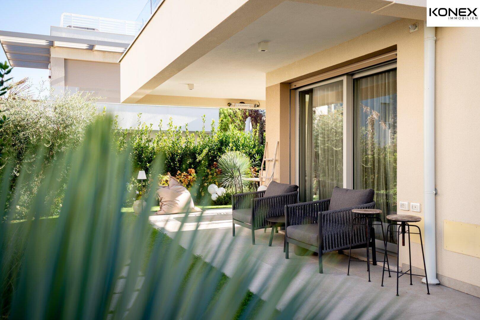 Überdachte Terrasse mit modernen Outdoor-Sesseln und Blick auf den grünen Garten.
