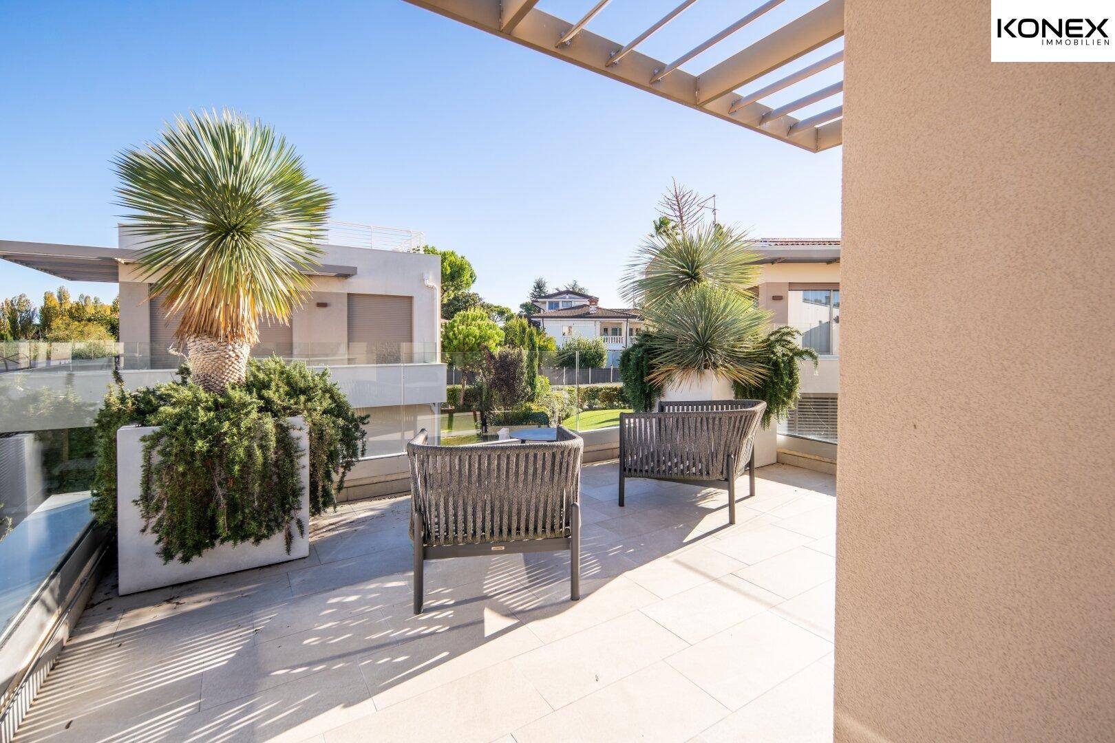Sonniger Balkon mit modernen Sitzgelegenheiten und dekorativen Pflanzen, ideal zum Entspannen.
