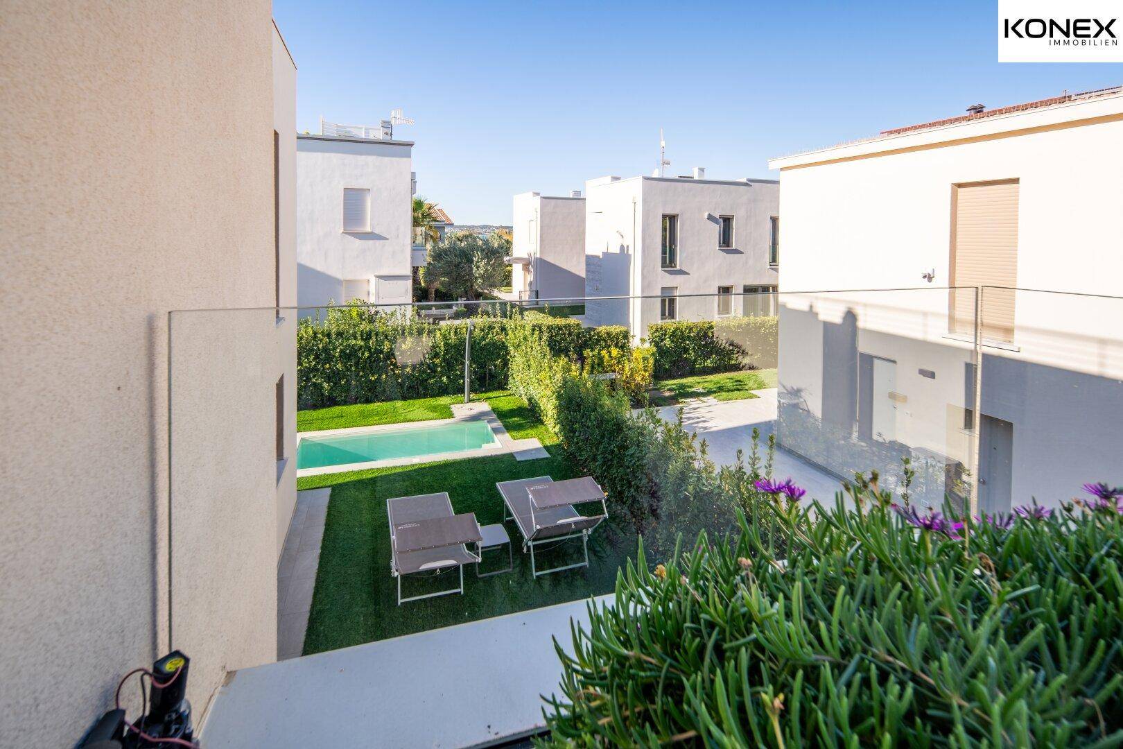Blick von oben auf den gepflegten Garten mit Pool und Liegestühlen, umgeben von Grün.
