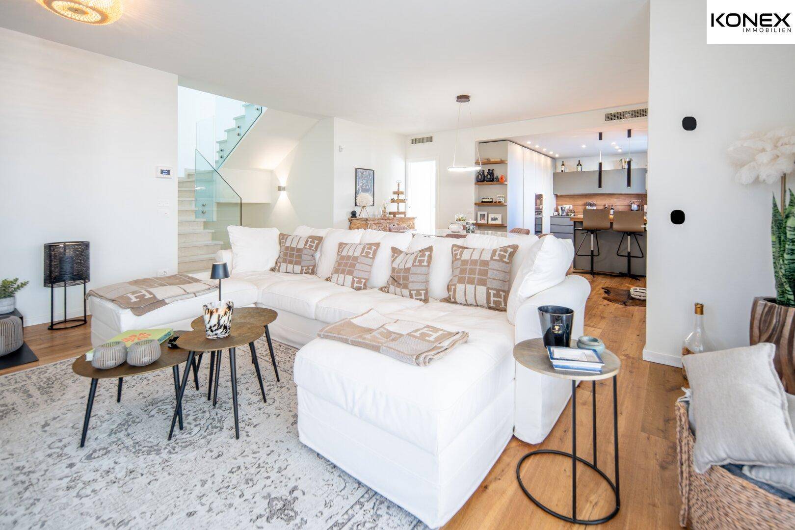 Helles Wohnzimmer mit großem weißen Sofa, Holzboden und offenem Übergang zum Essbereich und Treppenhaus.