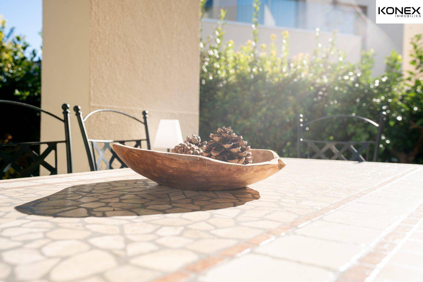 Detailaufnahme eines Terrassentisches mit Dekoration, umgeben von sonnigem Grün.