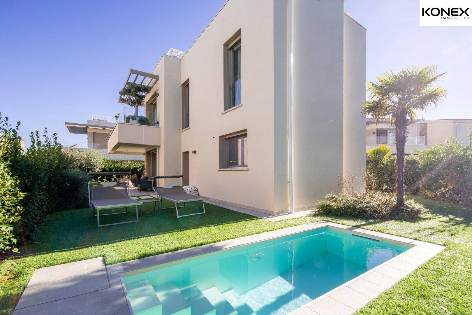 Moderner Garten mit kleinem Pool, Liegestühlen und gepflegtem Rasen neben dem Haus.