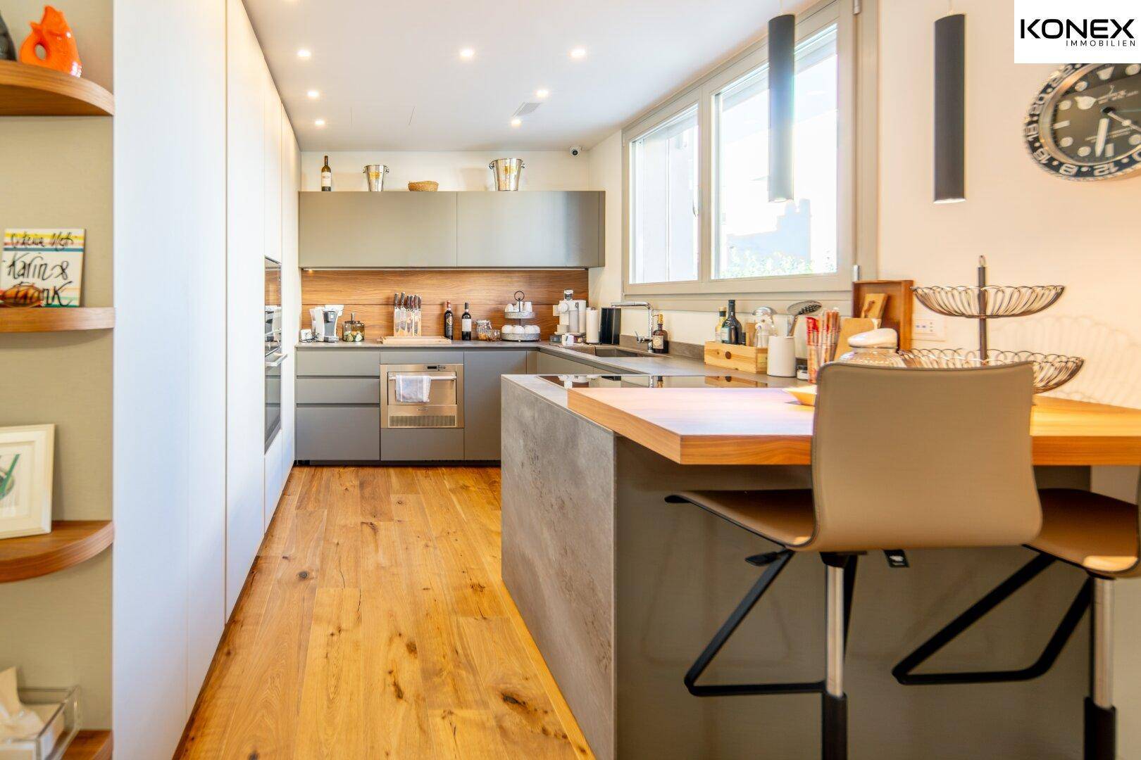 Moderne Küche mit Holzboden, grauen Schränken und einer Frühstücksbar, die zum Essbereich hin offen ist.