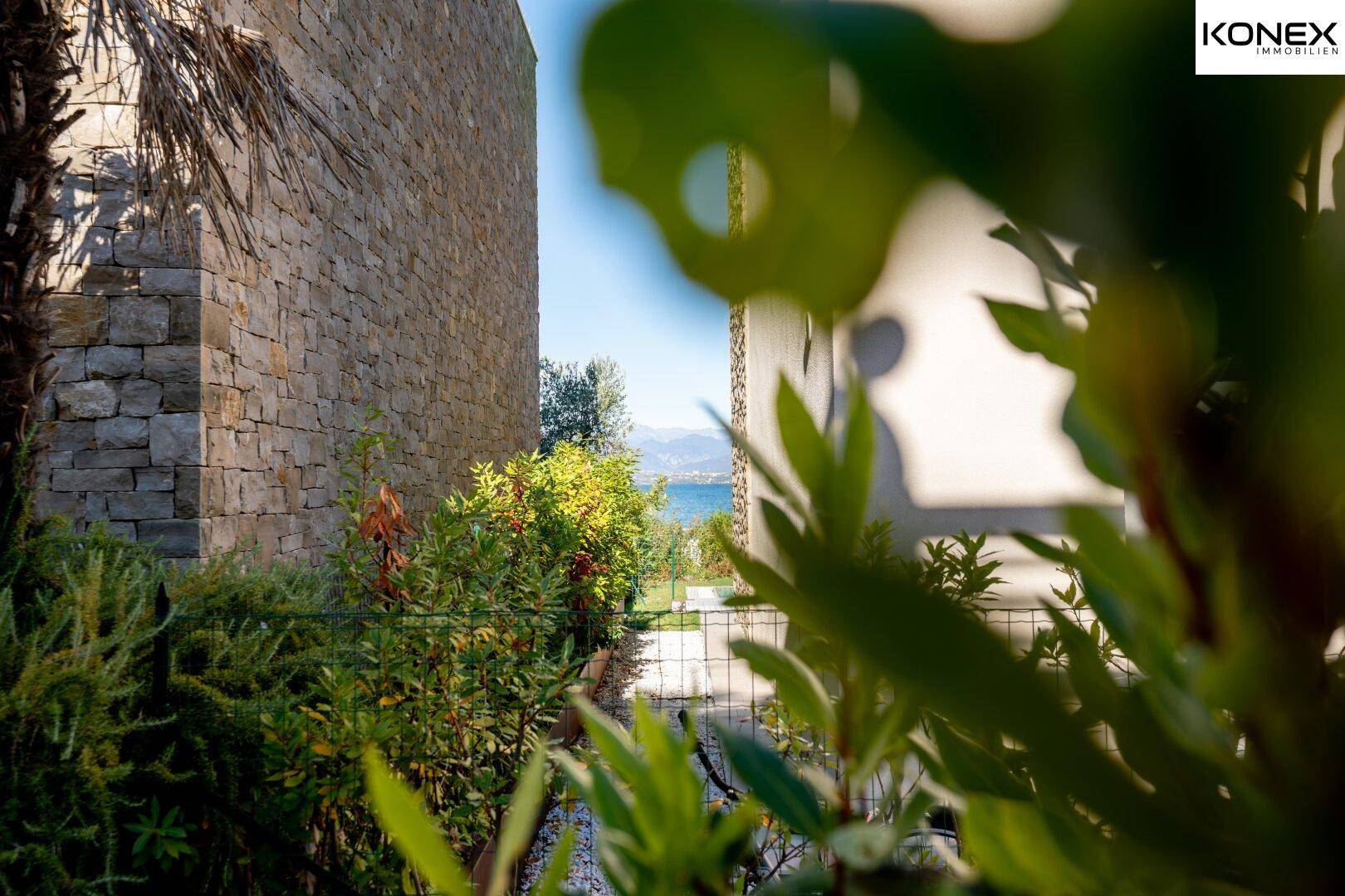 Seitlicher Blick auf die mediterrane Landschaft mit See im Hintergrund, durch Pflanzen gerahmt.