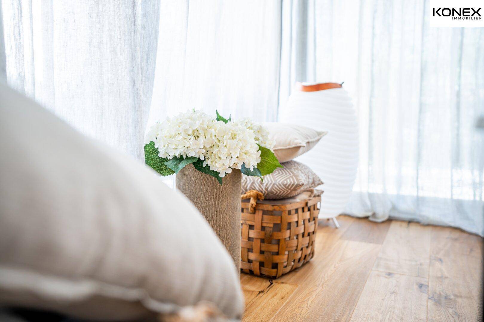 Detailaufnahme von Dekorationselementen im Wohnzimmer mit hellem Holzboden und Vorhängen.