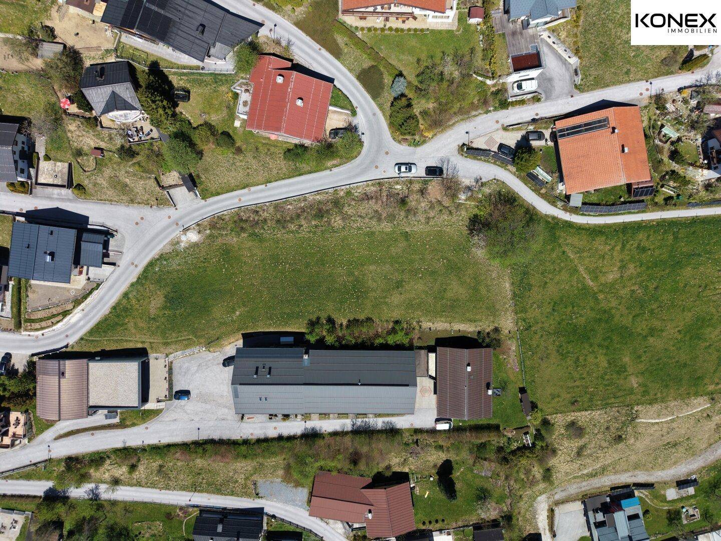 Draufsicht auf grüne Baugrundstücke und umliegende Straßen in einer ländlichen Umgebung.