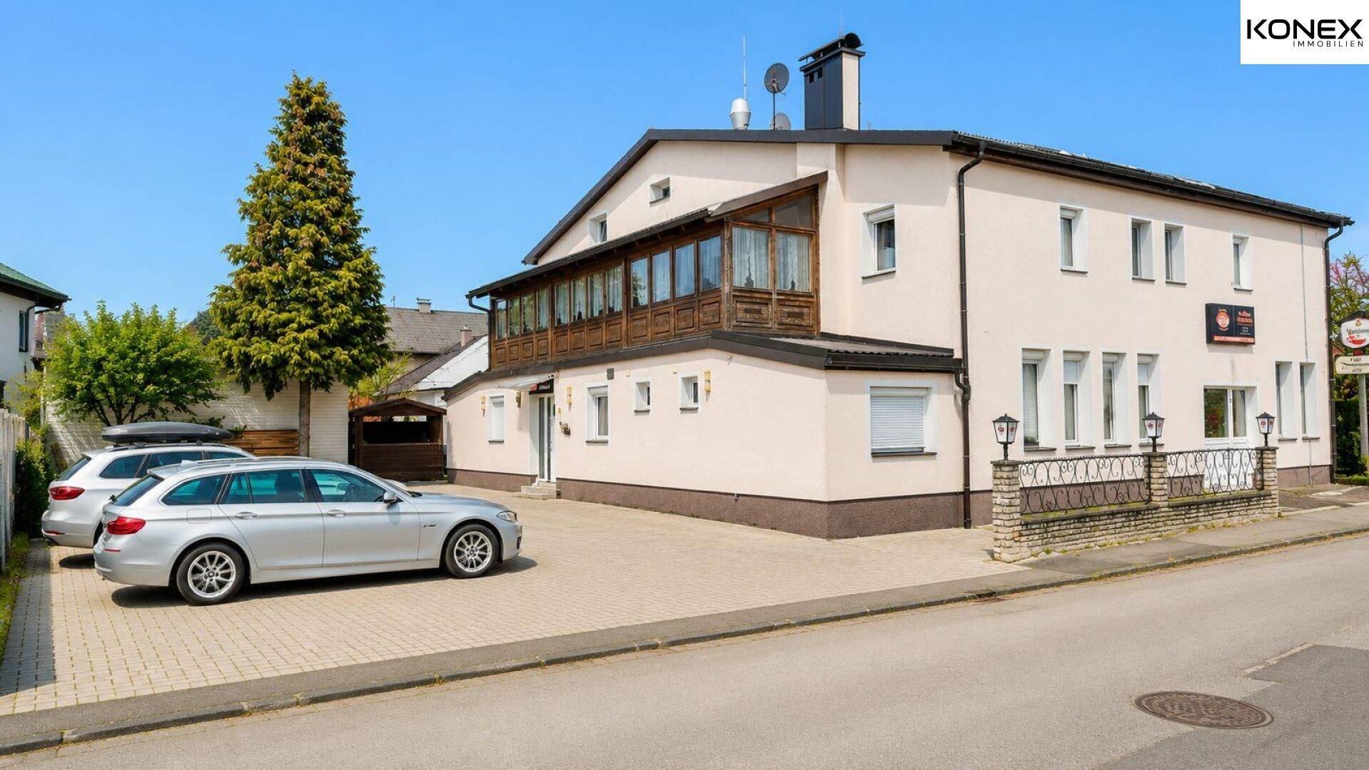 Gesamtansicht des Gebäudes mit großem Parkplatz und einem verglasten Wintergarten im Obergeschoss.