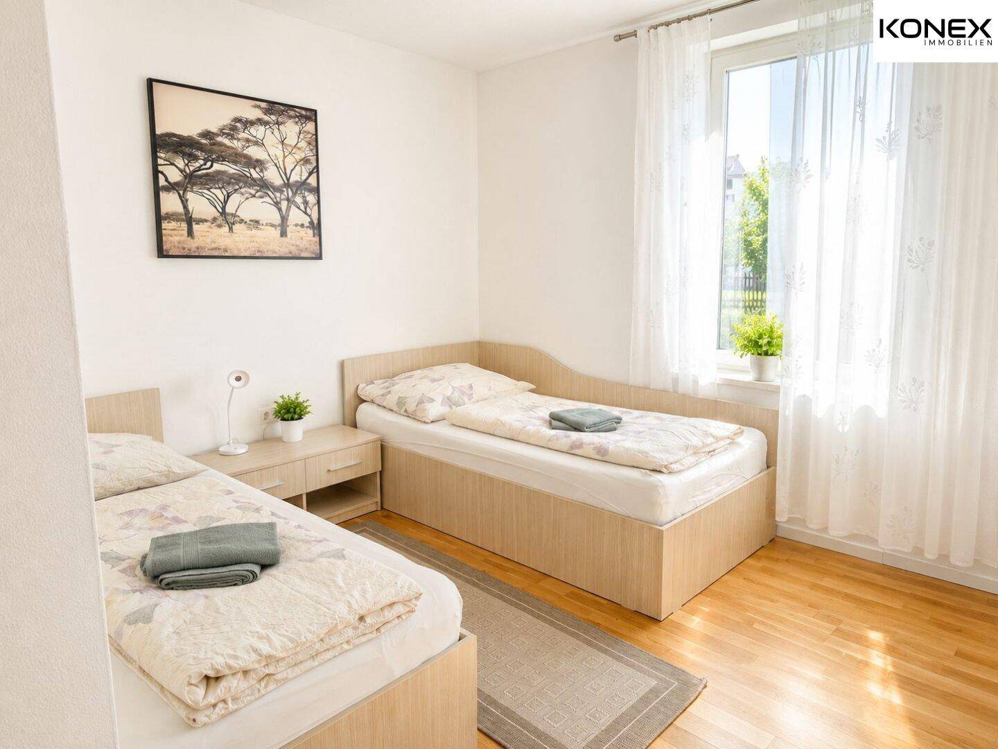 Helles Schlafzimmer mit zwei Einzelbetten, Holzfußboden und großem Fenster.