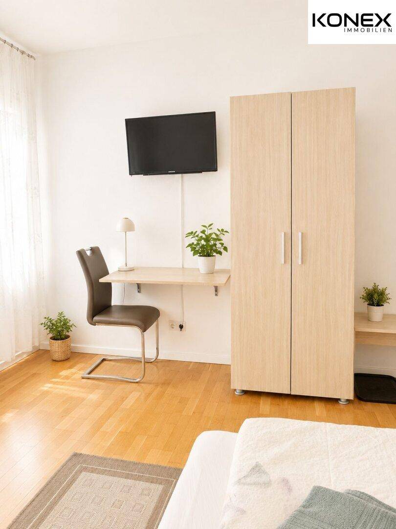 Schlafzimmer mit Holzboden, Wandfernseher, Schreibtisch und hellem Kleiderschrank.