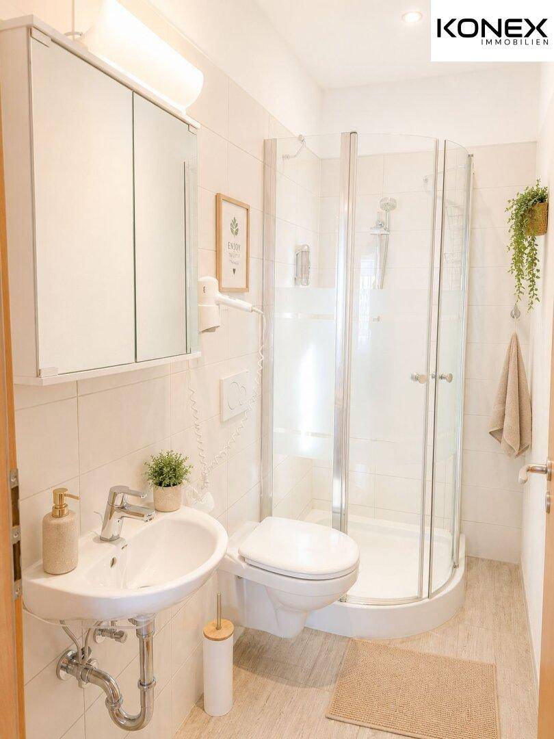 Helles Badezimmer mit Duschkabine, wandhängendem WC und einem Föhn an der Wand.