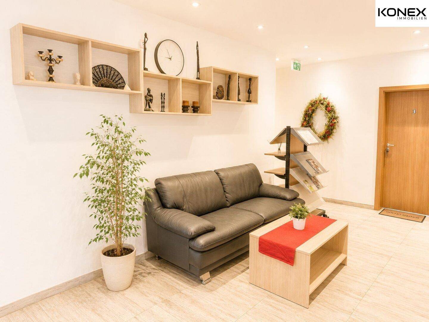 Einladender Empfangsbereich mit bequemer Ledercouch, Couchtisch und dekorativen Regalen.