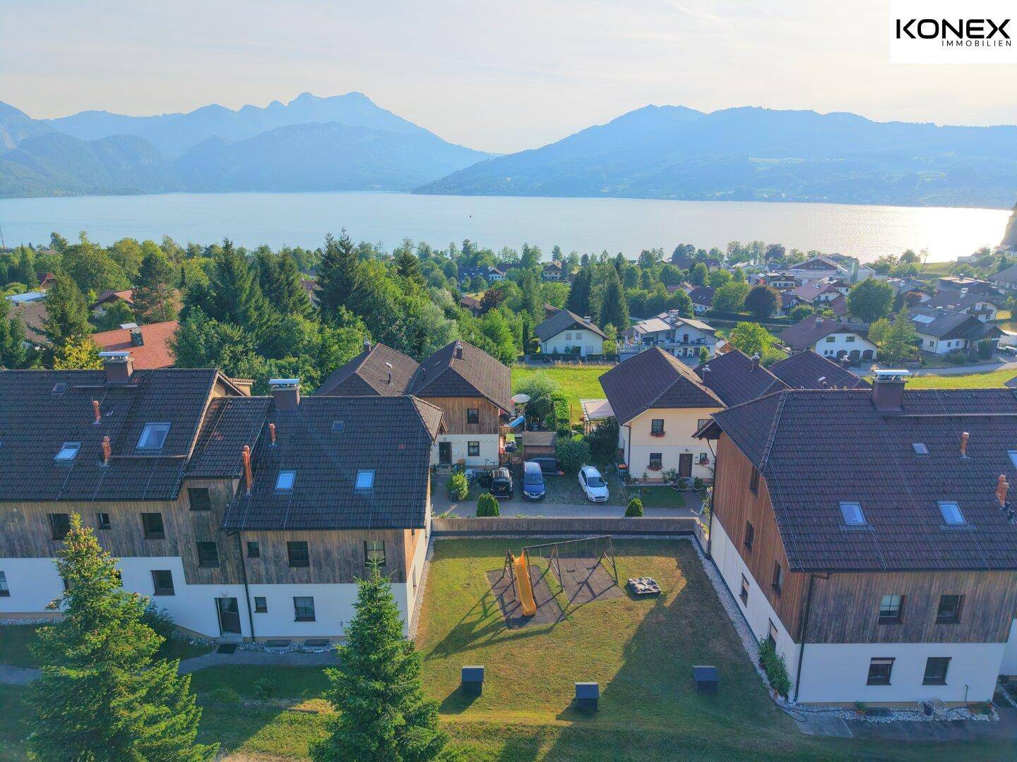 Überblick über die Wohnanlage mit See- und Bergkulisse und einem gemeinschaftlichen Spielplatz.