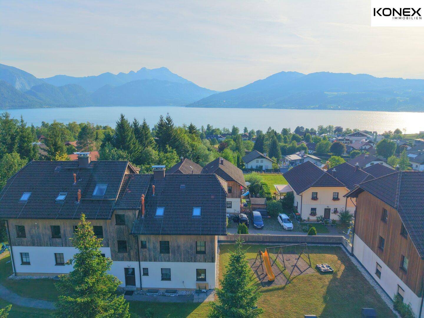 Luftaufnahme der Wohnanlage mit See- und Bergblick sowie einem Spielplatzbereich.