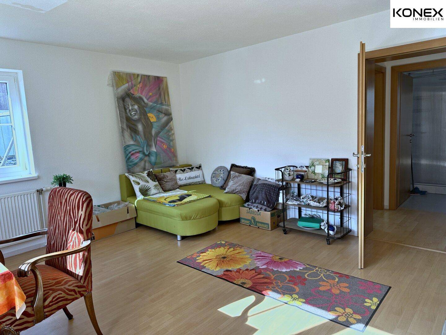 Wohnzimmer mit bequemer grüner Couch, farbenfrohem Teppich und hellem Laminatboden.