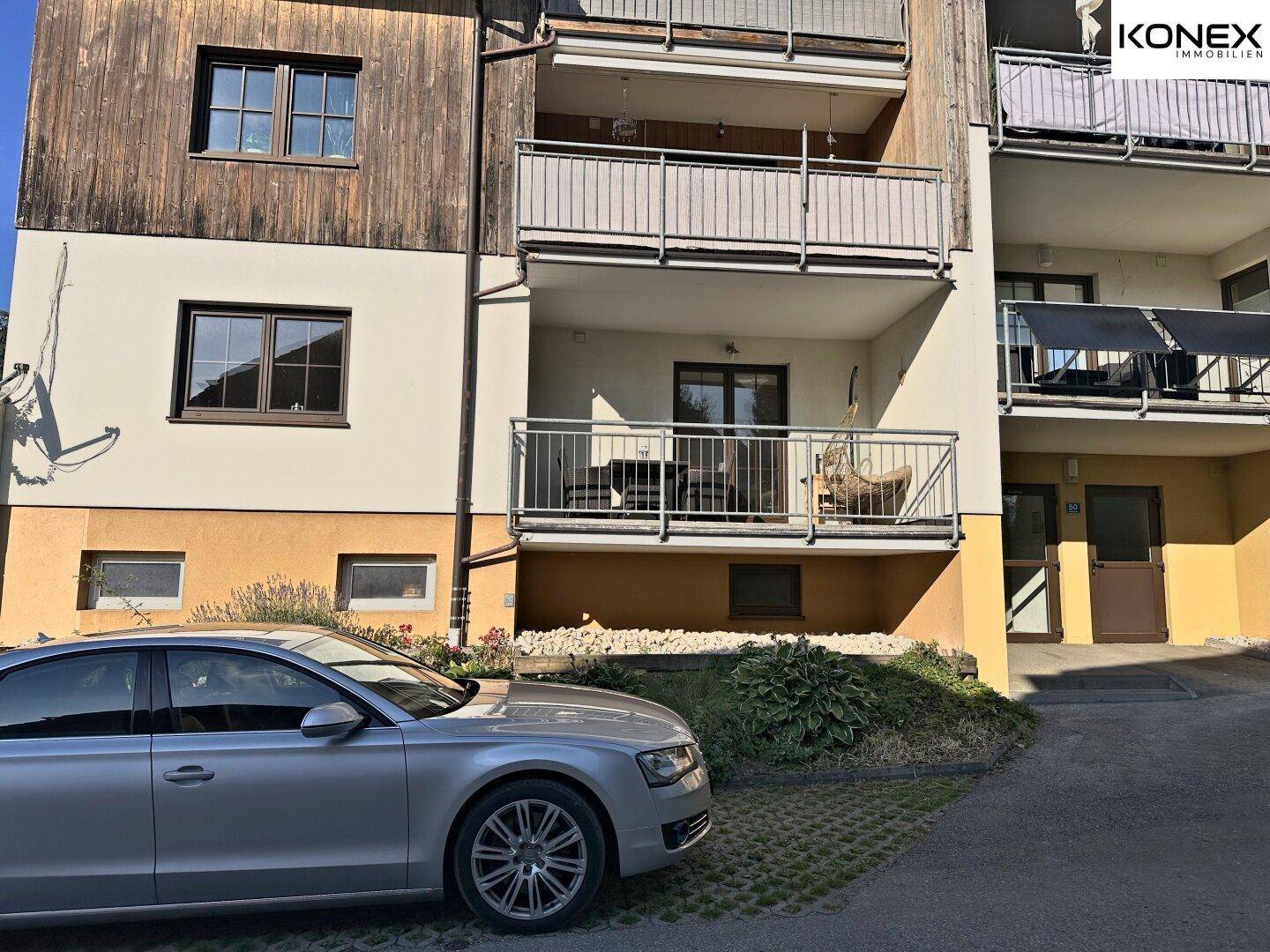 Vorderansicht des Gebäudes mit Balkonen und einem geparkten Auto auf dem Vorplatz.