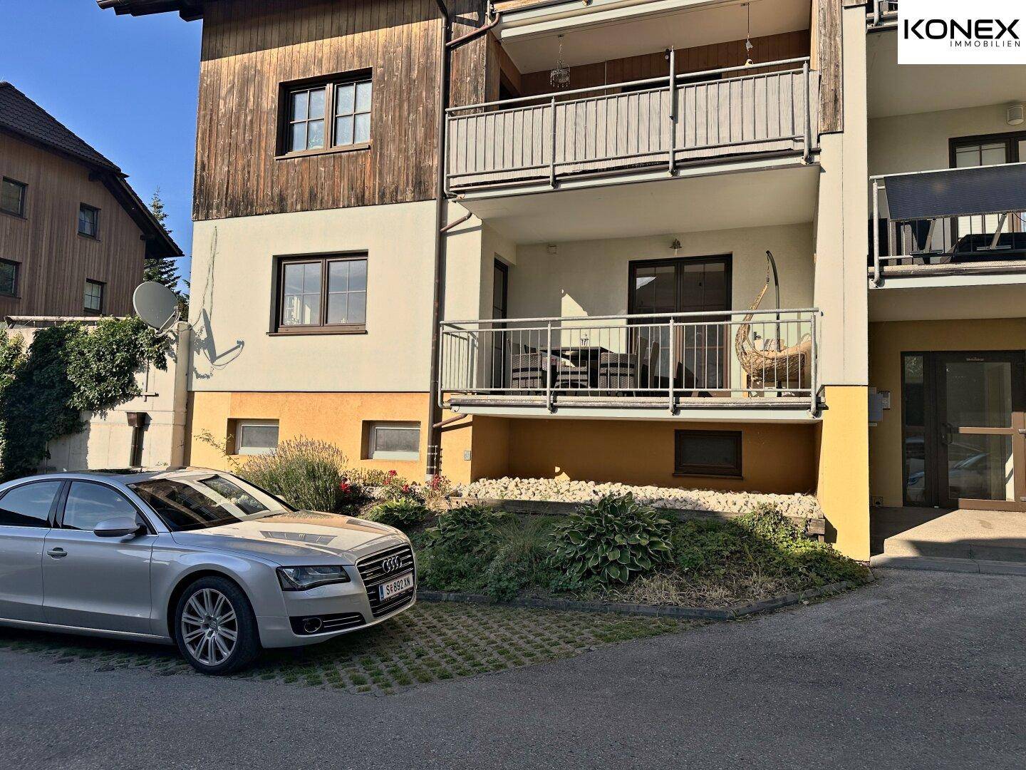 Gebäudeansicht mit Balkonen und einem geparkten Fahrzeug auf dem gepflasterten Parkplatz.