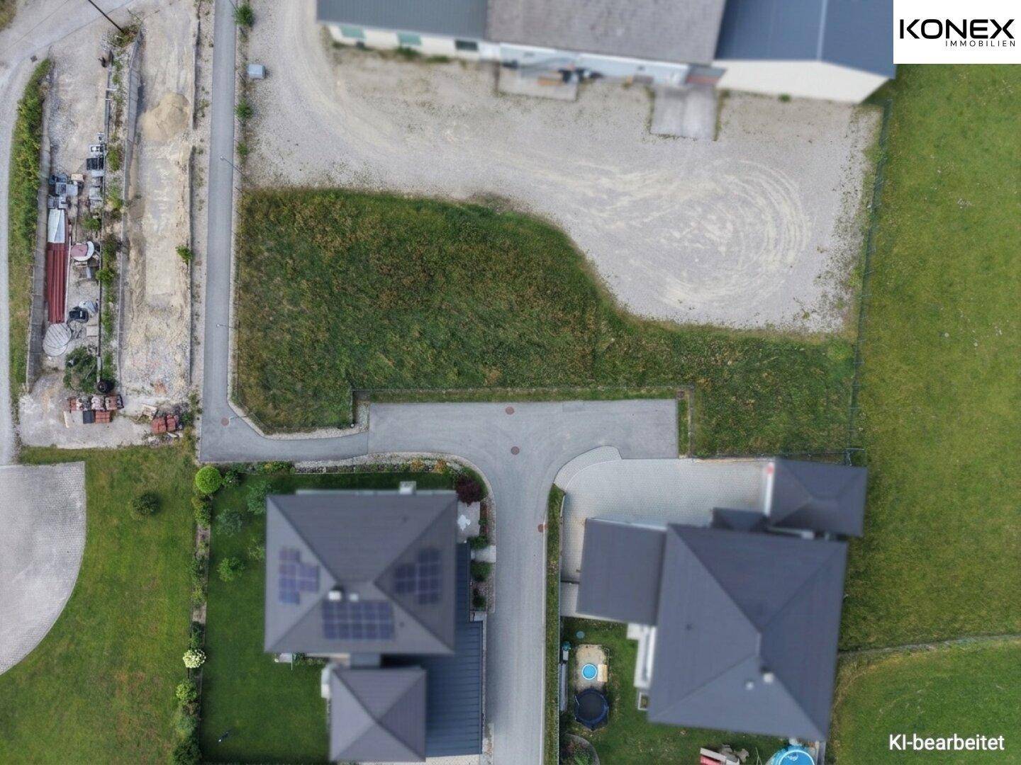 Vogelperspektive auf Dächer von Wohnhäusern, Straßen und grüne Flächen in einer ländlichen Umgebung.