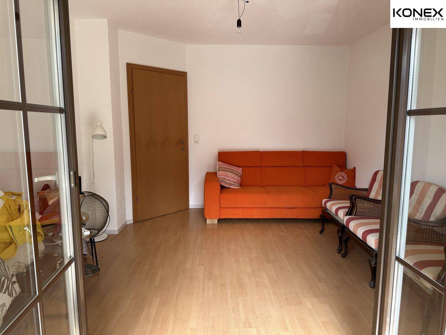 Helles Wohnzimmer mit orangefarbenem Sofa und Laminatboden, gesehen durch eine Glastür.