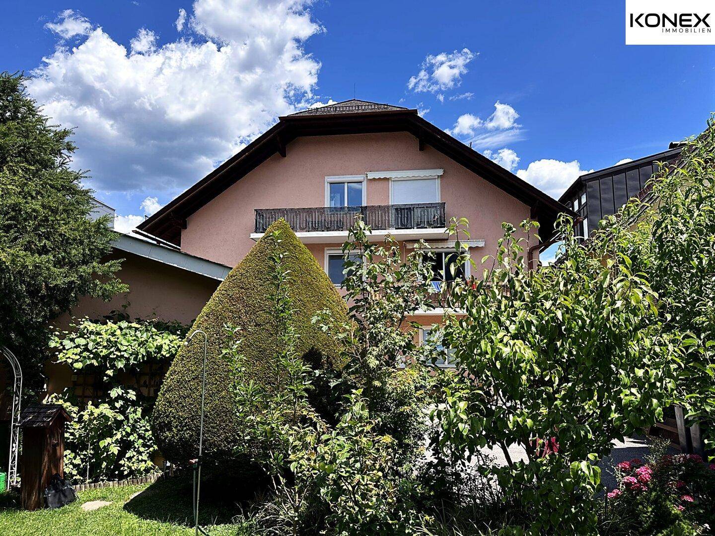Wohnhausansicht vom Garten aus, umgeben von üppiger Vegetation und Bäumen.