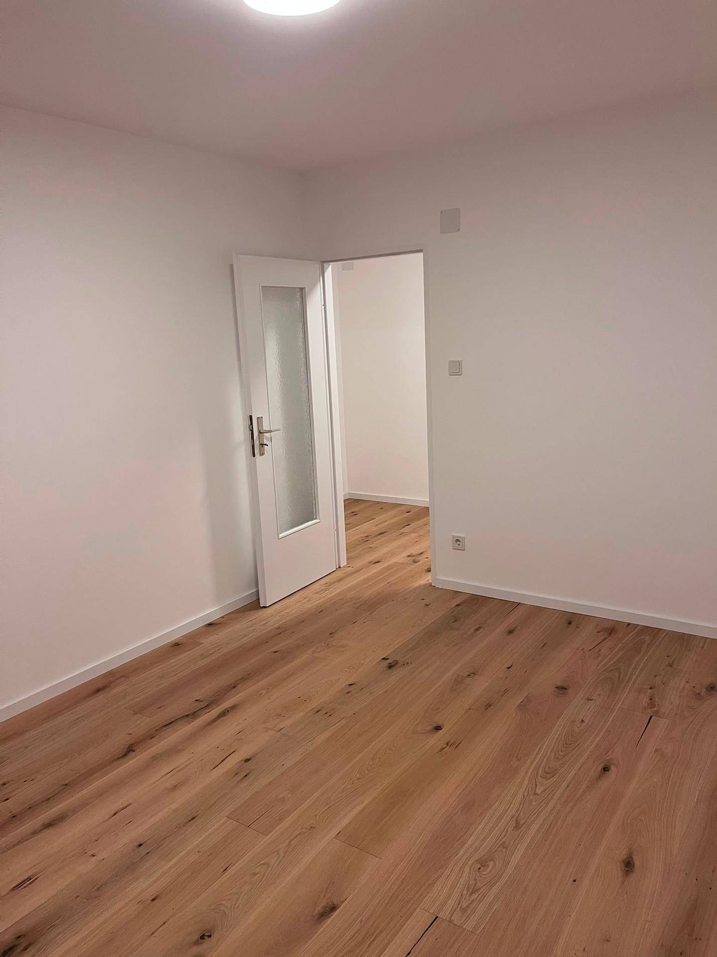 Geräumiges Zimmer mit Holzboden und einer Tür, die zu einem weiteren Raum führt.