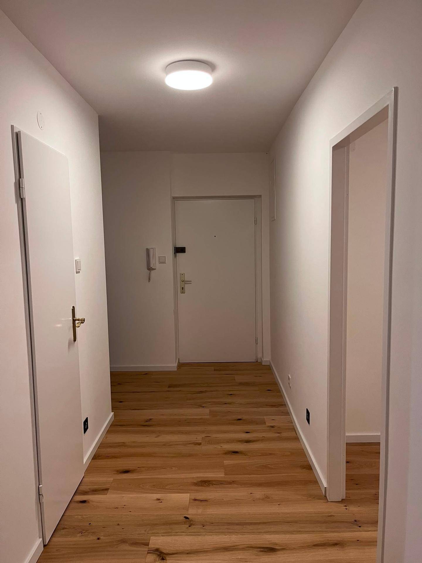 Langer, heller Flur mit Holzboden und weißen Wänden, der zu verschiedenen Räumen führt.