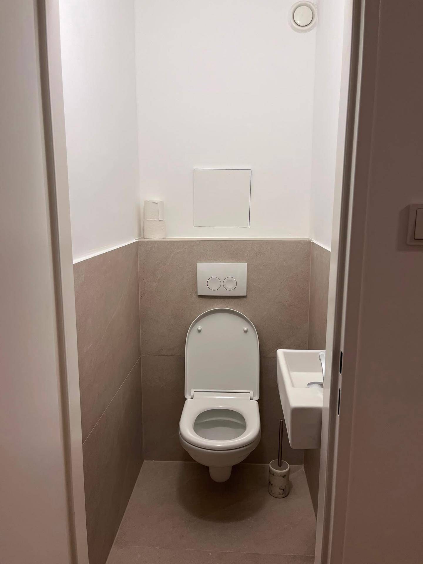 Modernes Gäste-WC mit Wand-WC, kleinem Waschbecken und hellen Fliesen.