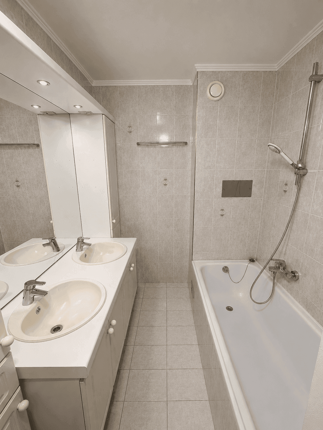 Gefliestes Badezimmer mit Doppelwaschbecken, Badewanne und Spiegelschrank.