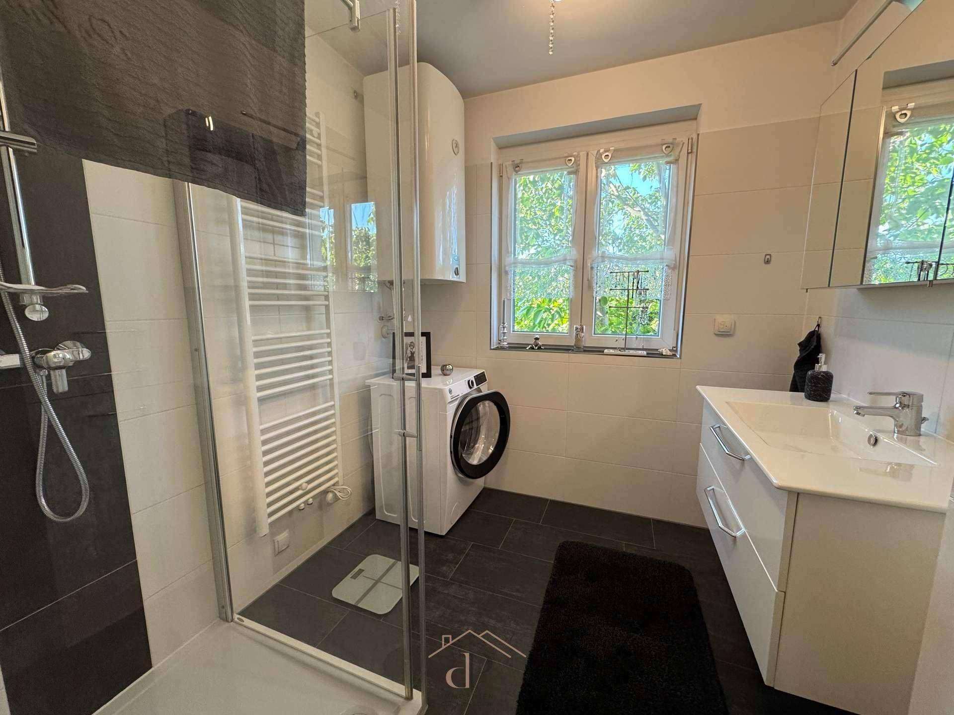 Modernes Badezimmer mit ebenerdiger Dusche, Waschmaschine und Fenster.