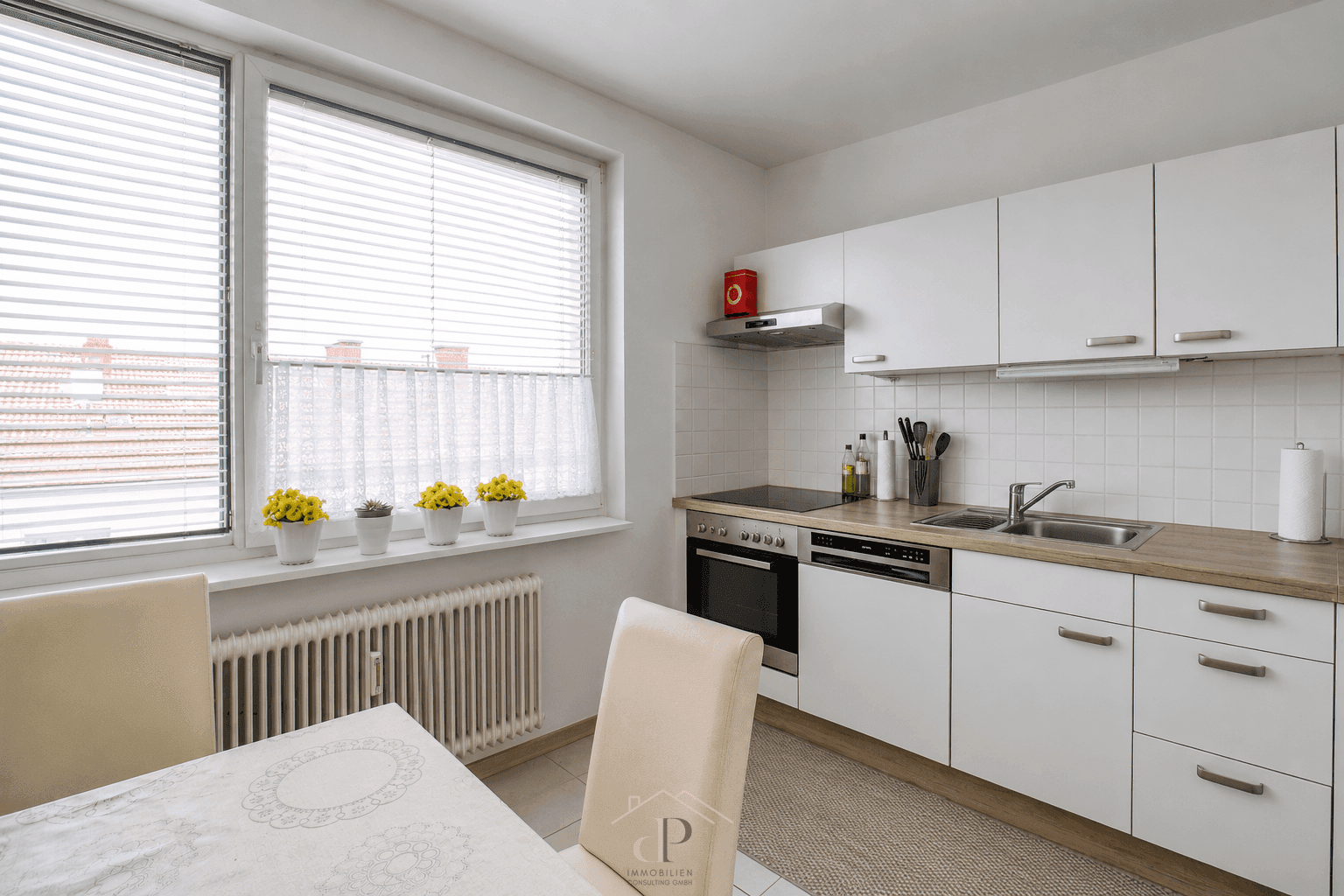 Helle Küche mit weißen Schränken, Holzarbeitsplatte und Essbereich am Fenster mit Blick auf Dächer.