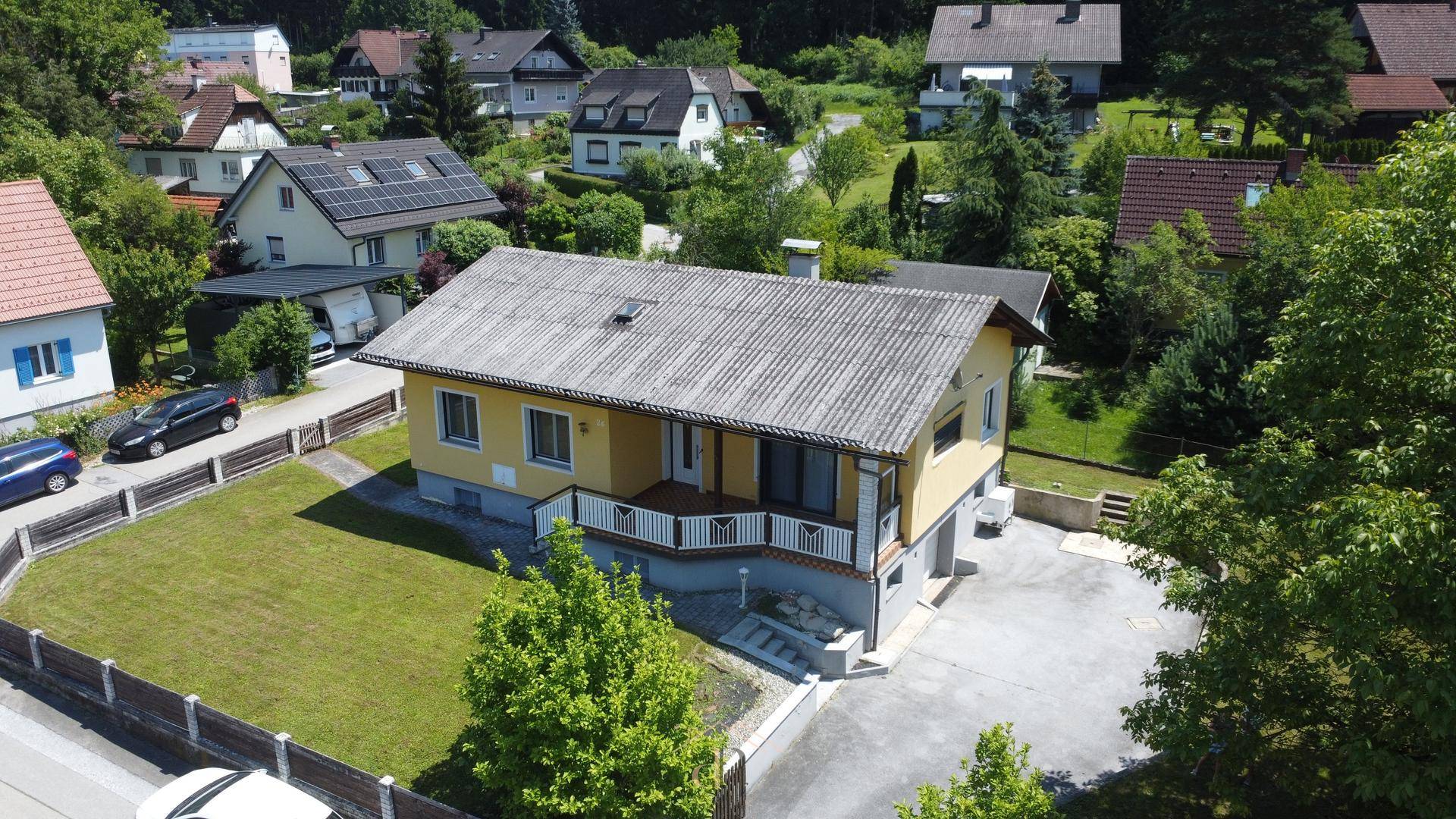 Luftaufnahme eines Einfamilienhauses mit Garten und umliegender Wohnbebauung in grüner Umgebung.