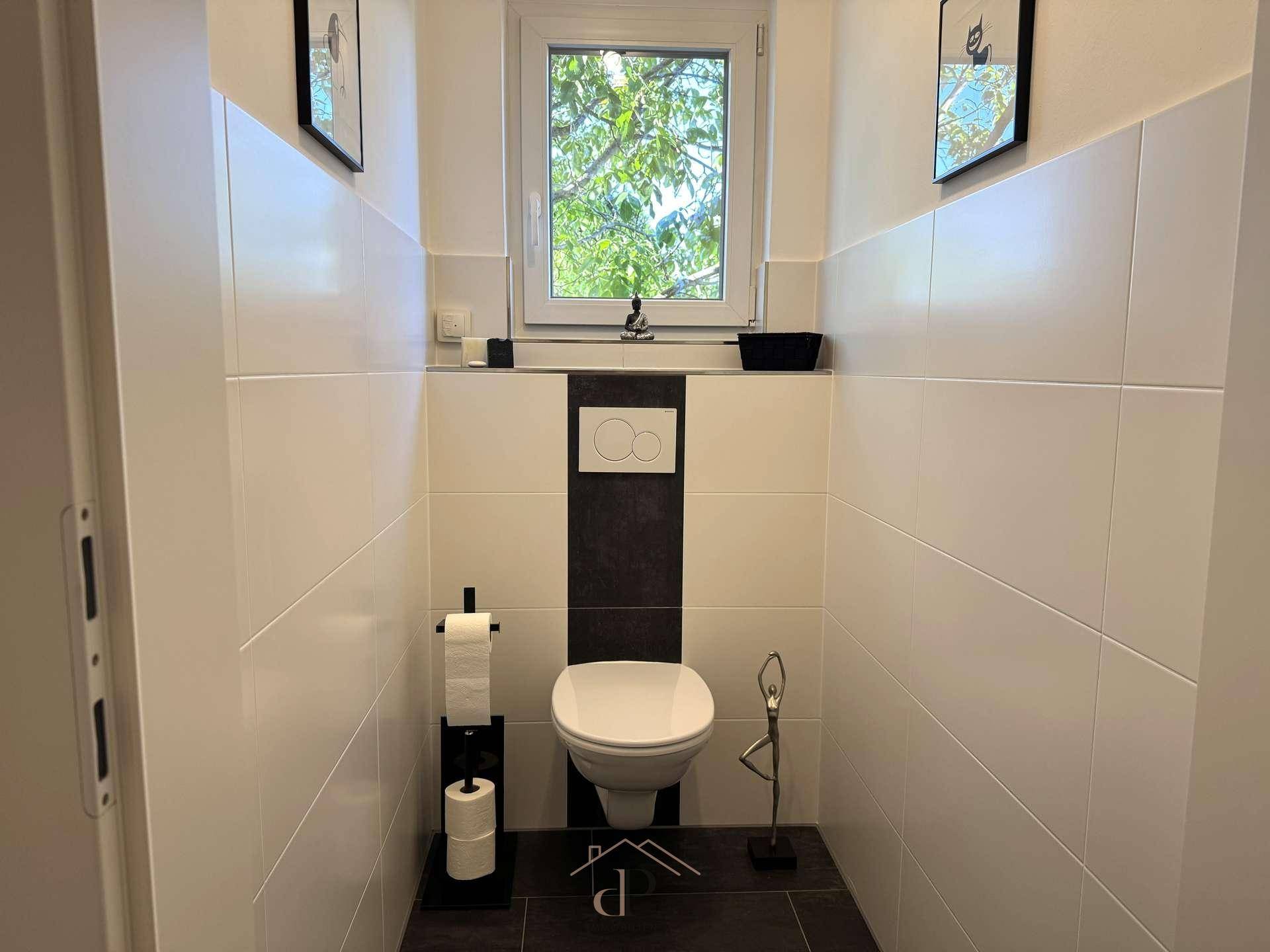 Separates Gäste-WC mit wandhängender Toilette und Fenster für natürliche Belüftung.