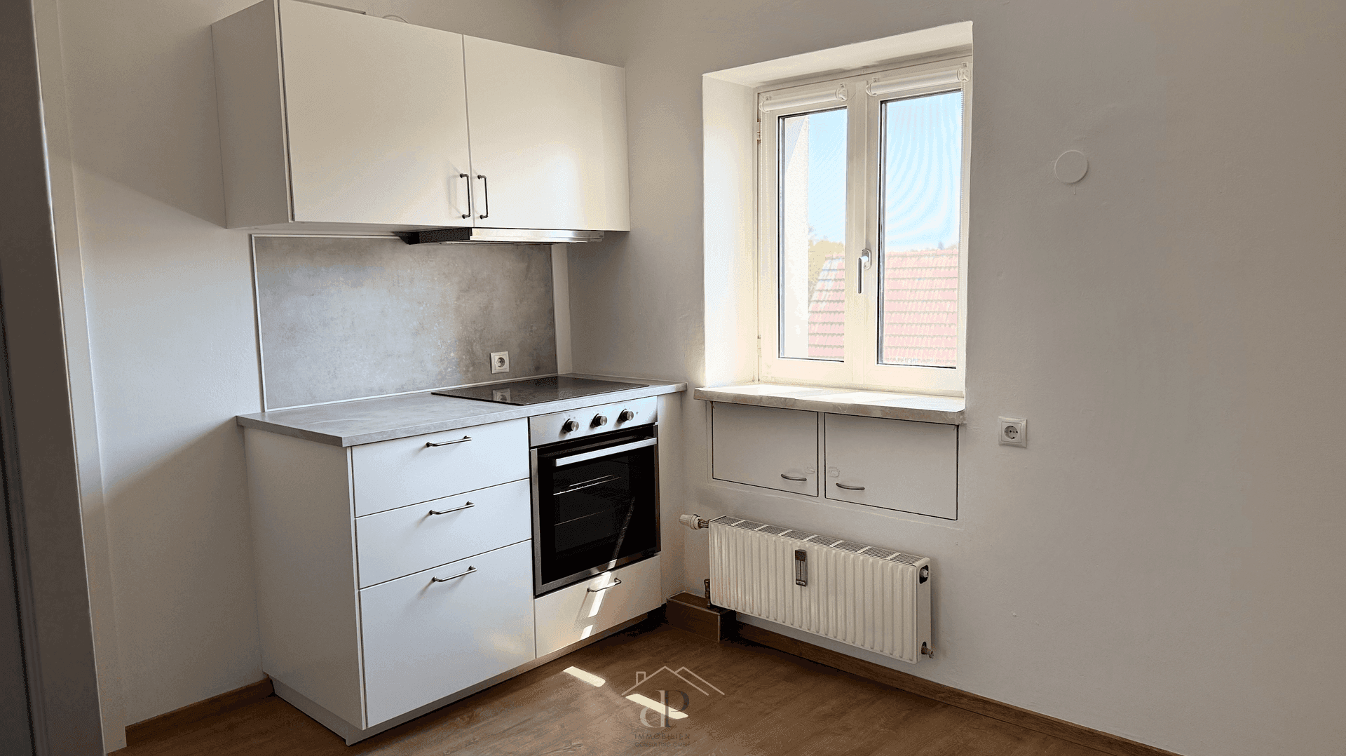 Kompakte Küchenzeile mit Kochfeld, Backofen und Fenster, ideal für kleine Wohnungen.