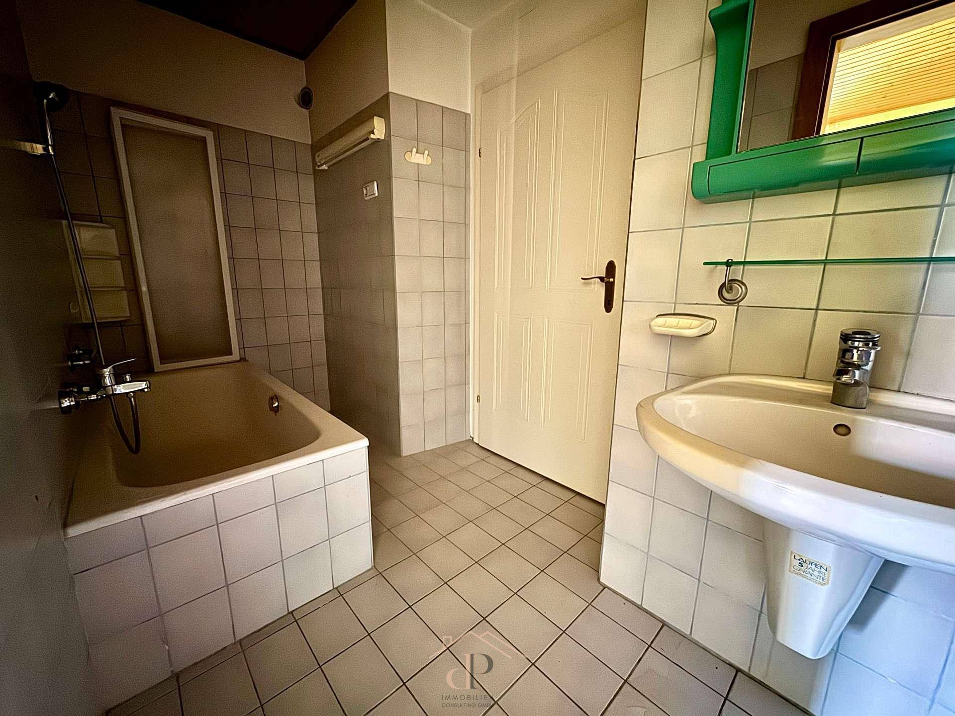 Badezimmer mit Badewanne, Waschbecken und hellen Fliesen, im Stil der 80er Jahre.