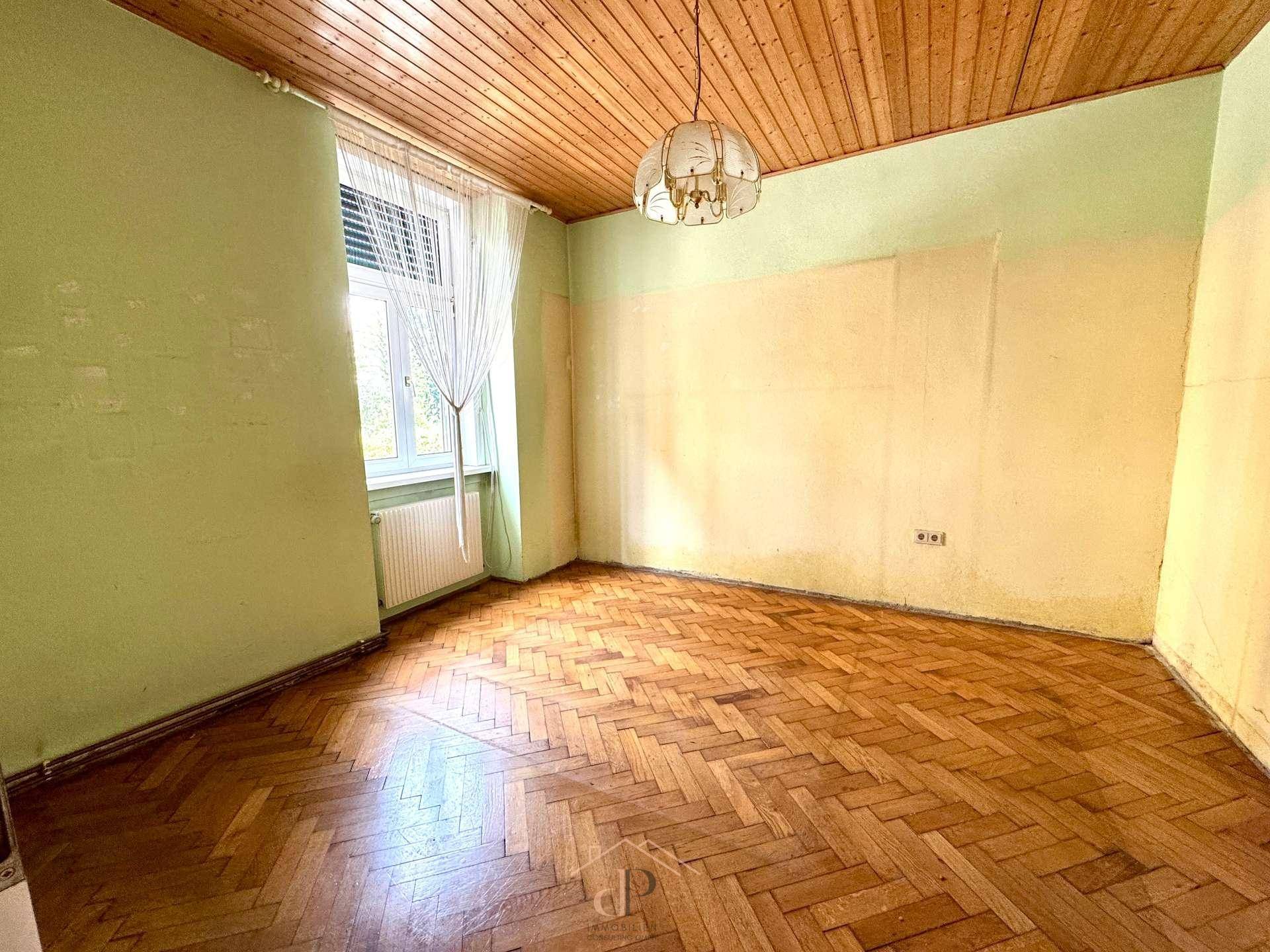 Helles Zimmer mit Holzdeckenverkleidung und Fischgrätparkett, mit Blick ins Grüne.