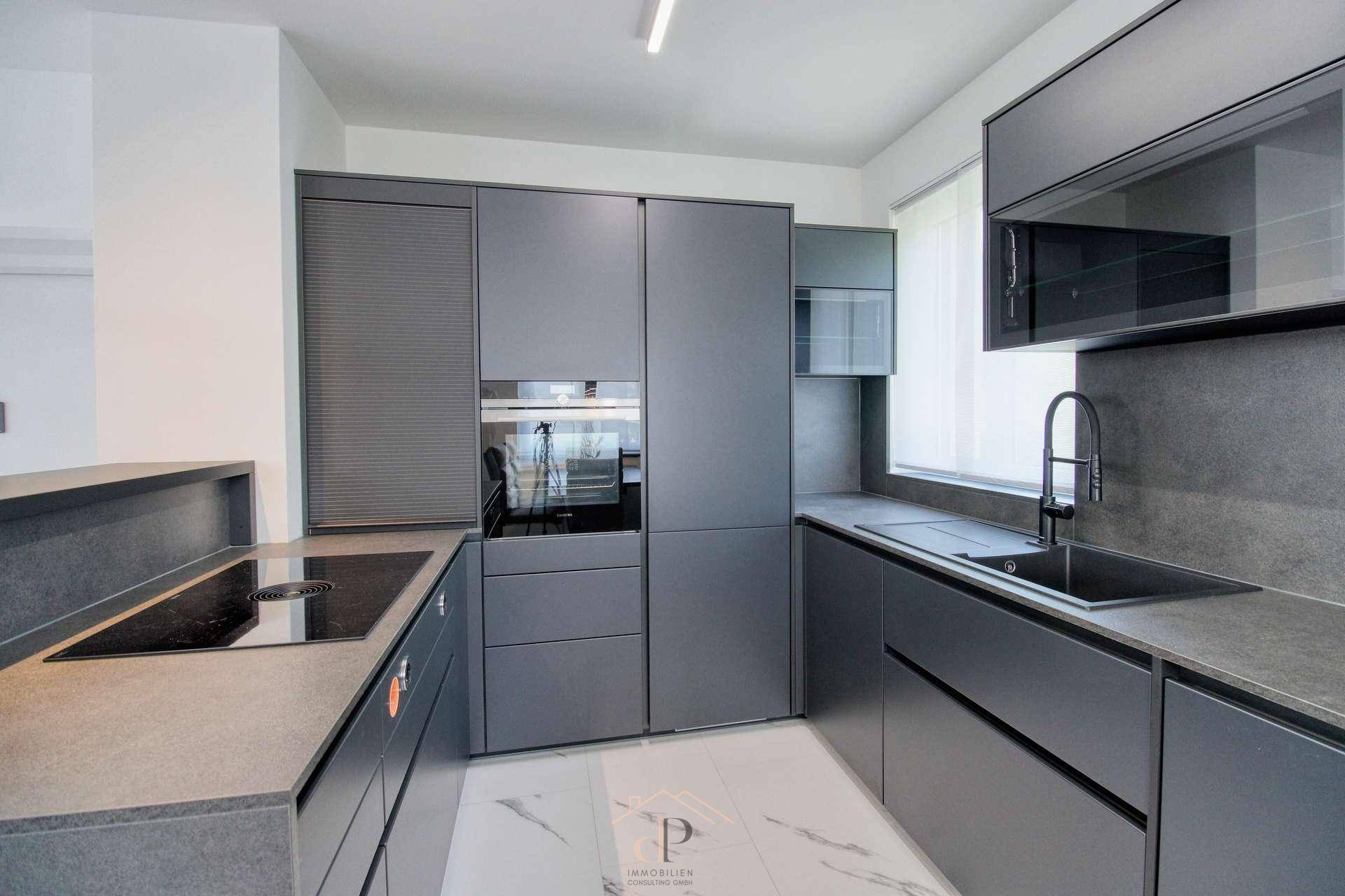 Moderne Küche mit grauen Fronten, Induktionskochfeld und integrierten Premium-Geräten auf Marmorboden.