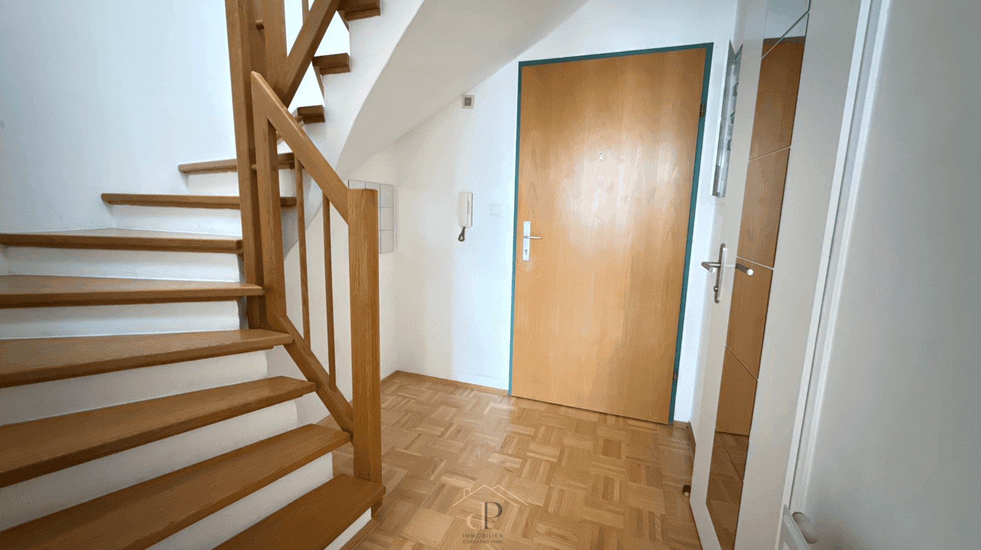 Heller Eingangsbereich mit Holztreppe, Parkettboden und einer Holztür.
