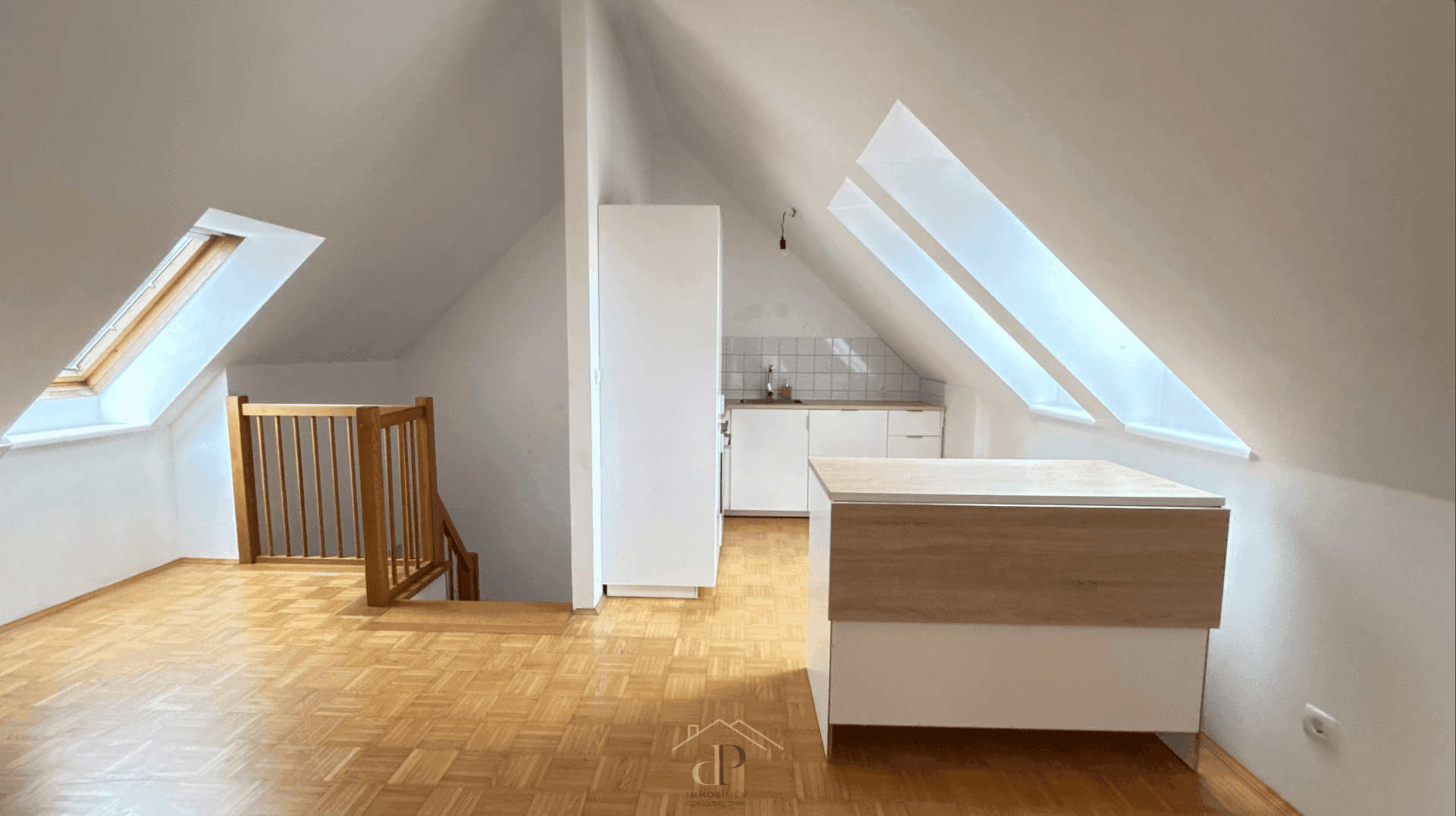 Offener Wohnbereich im Dachgeschoss mit kleiner Küchenzeile, Holztreppe und Dachfenstern.