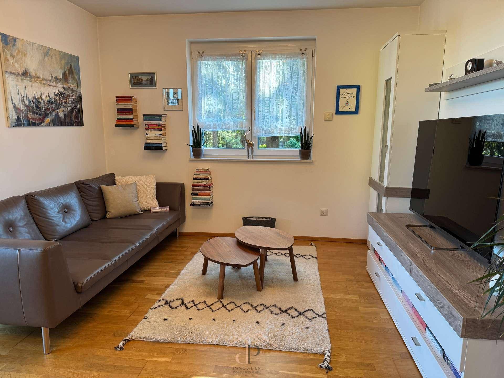 Gemütliches Wohnzimmer mit bequemer Couch, Couchtischen und Blick ins Grüne.