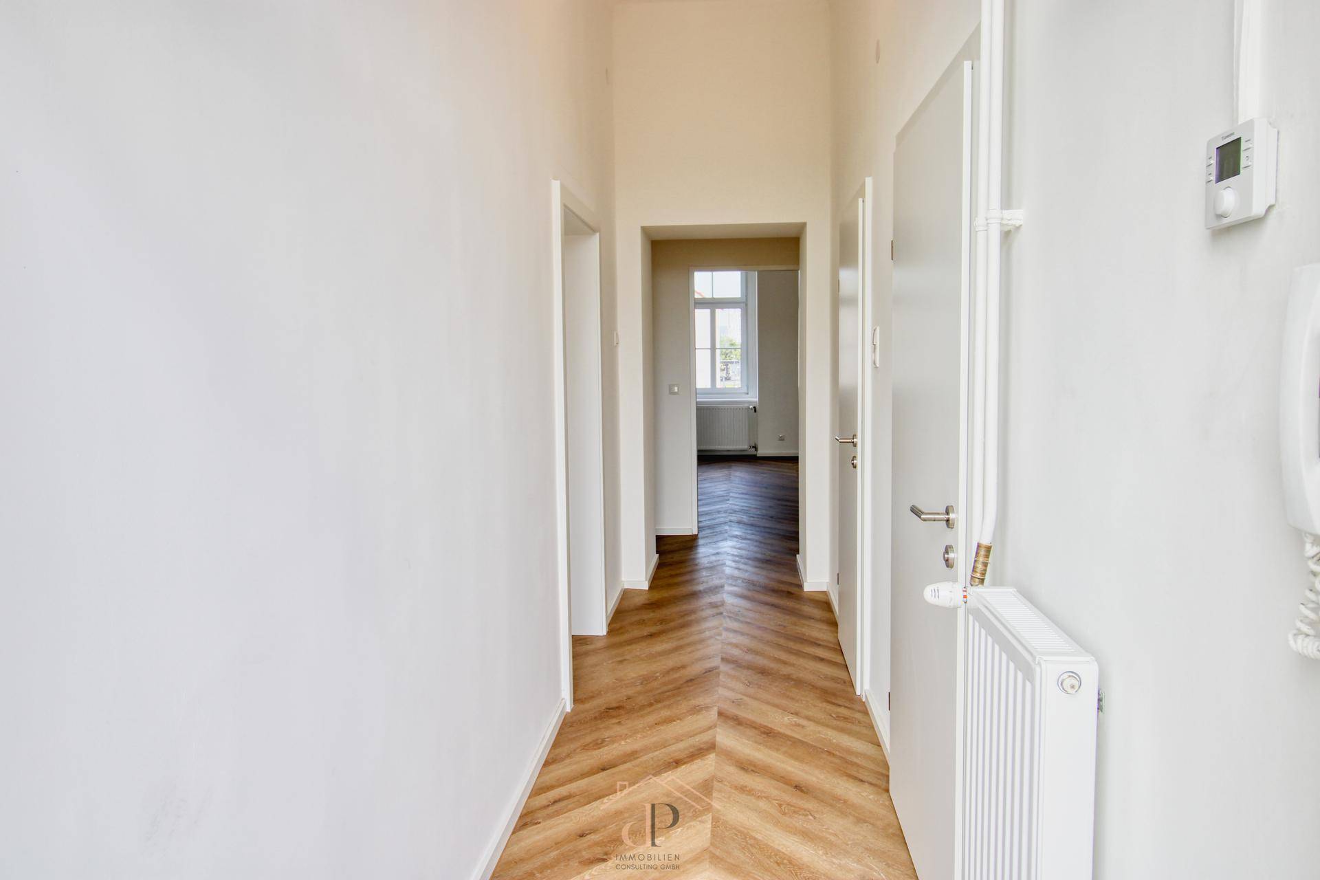 Heller Flur mit Fischgrätparkett, weißen Wänden und Zugang zu weiteren Räumen der Wohnung.