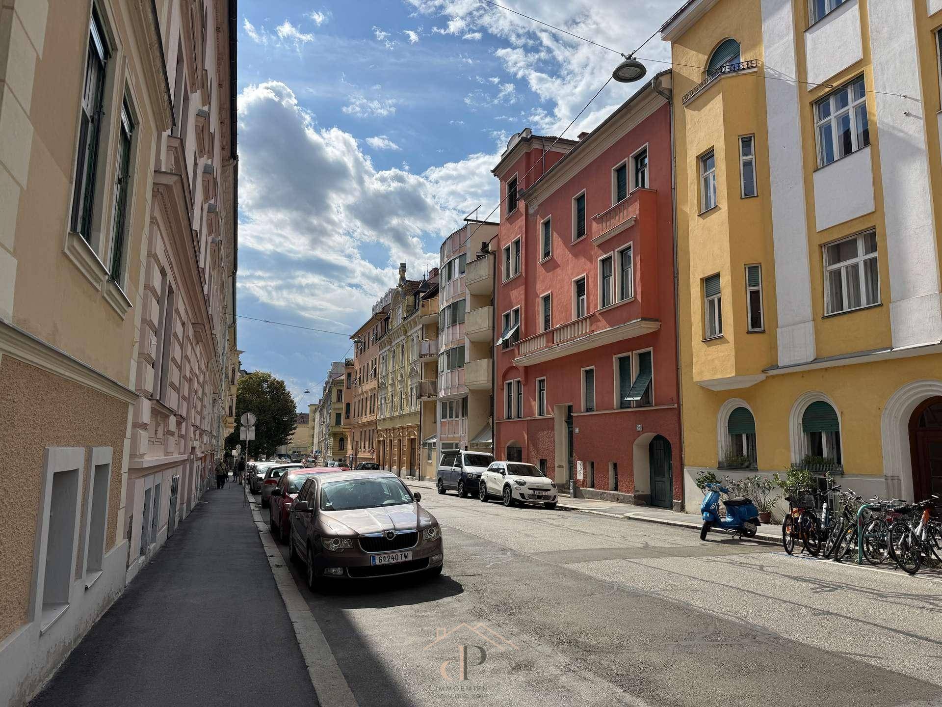 Malerische Stadtstraße mit historischen Gebäuden und parkenden Autos unter blauem Himmel.