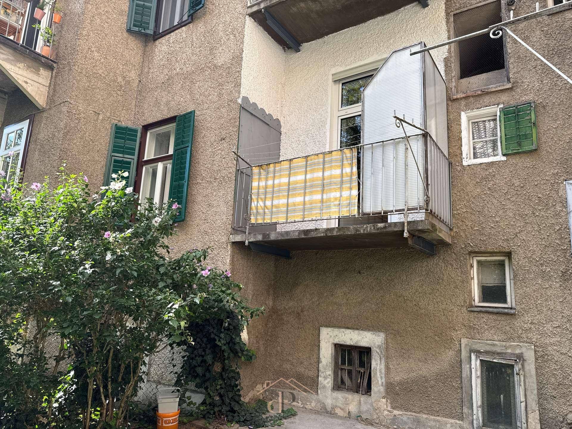 Rückansicht des Gebäudes mit Balkon und grüner Bepflanzung im Innenhof.
