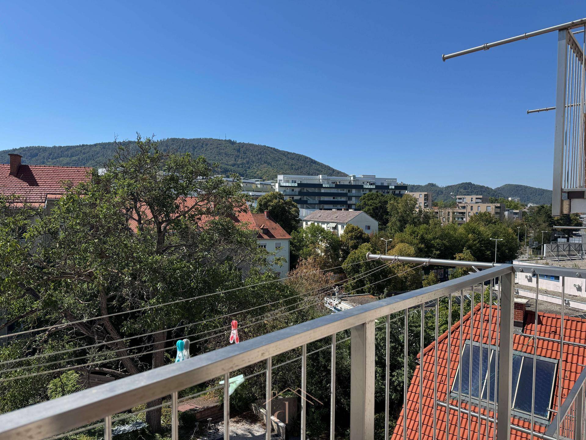 Balkon mit weitem Blick über die Dächer der Stadt und die bewaldeten Hügel im Hintergrund.