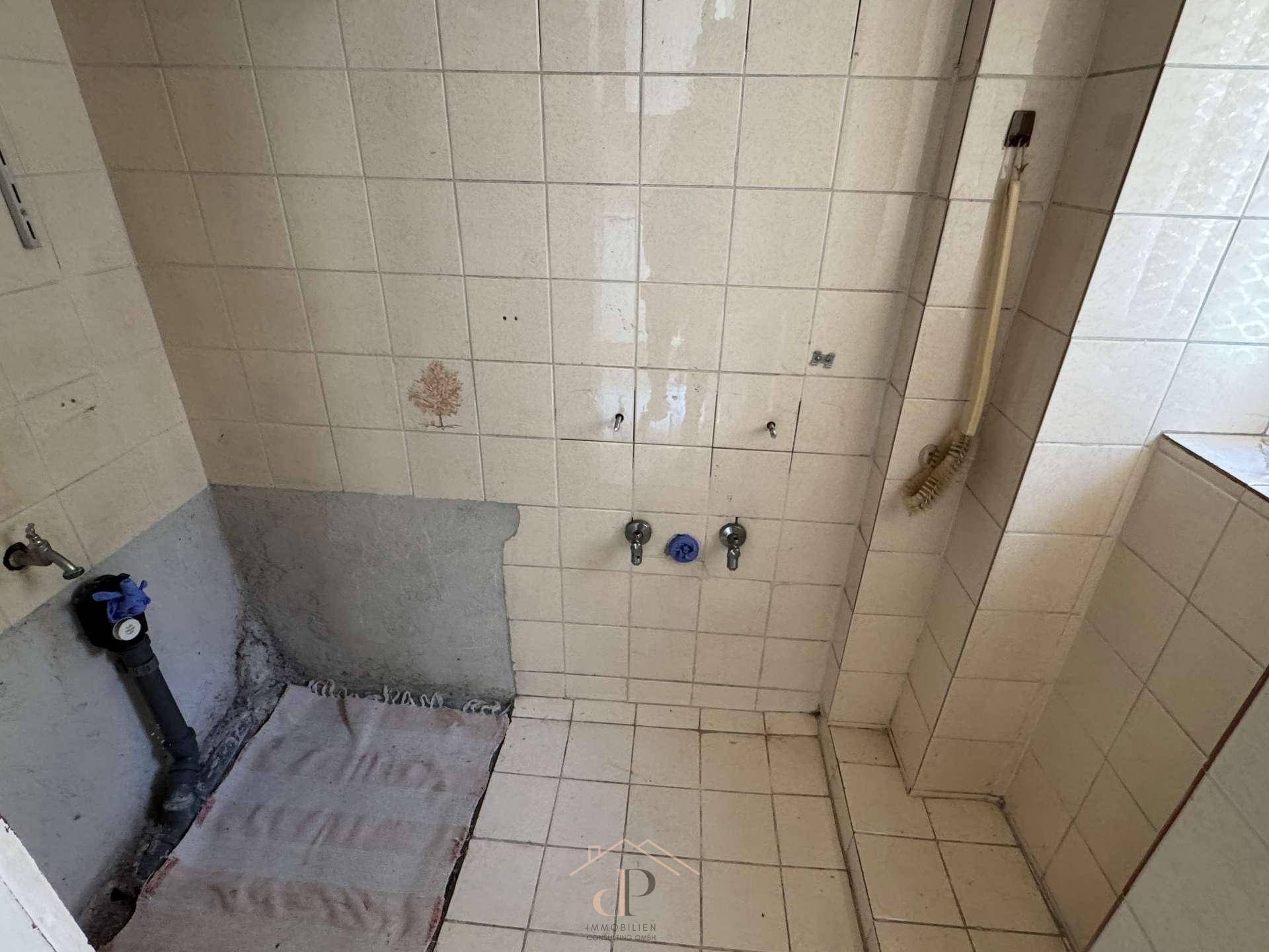 Einfacher Raum mit Fliesenboden und Anschlüssen, ideal für eine zukünftige Waschküche oder Küche.