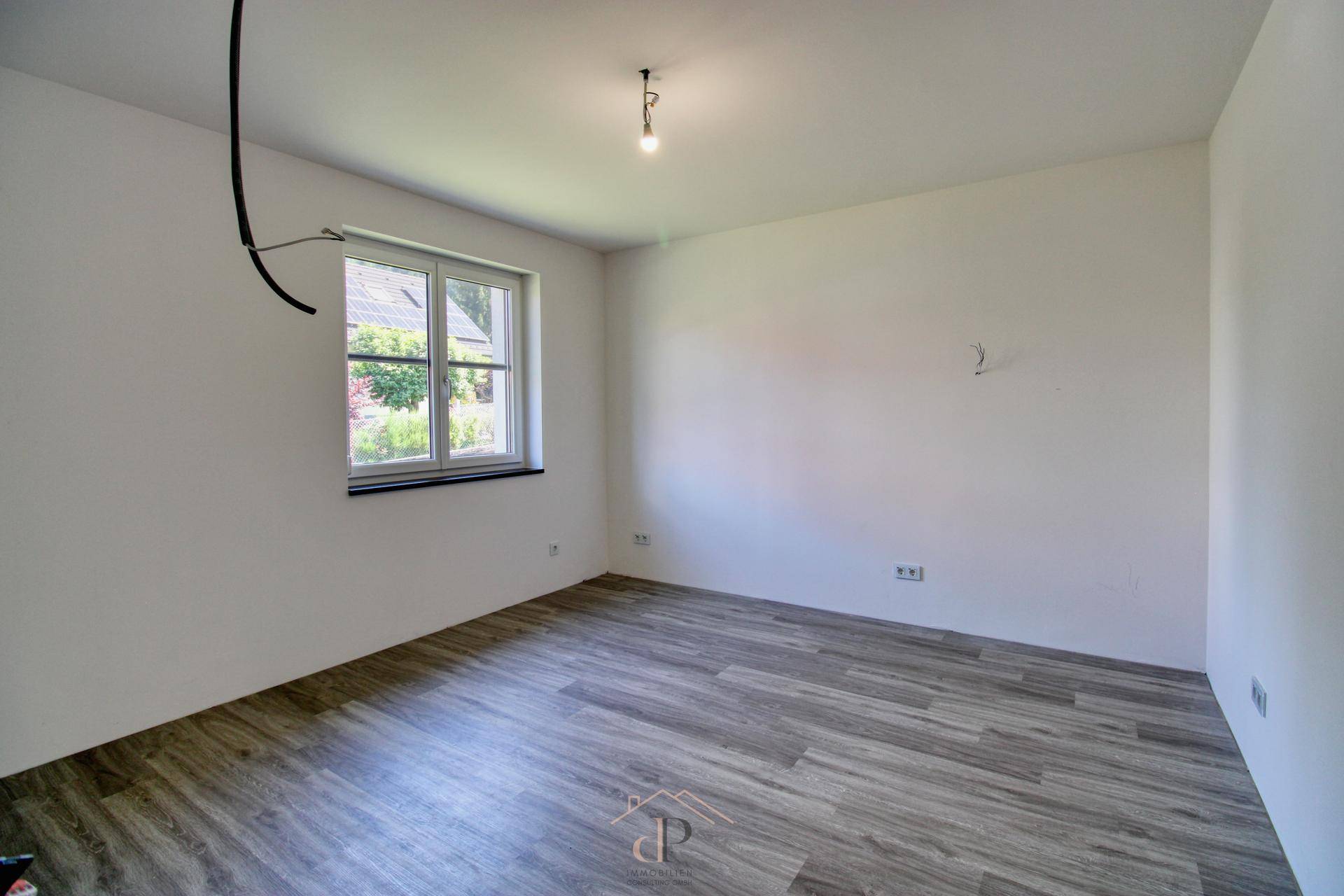 Leerer Raum mit Laminatboden und einem Fenster, bereit zur individuellen Gestaltung und Nutzung.