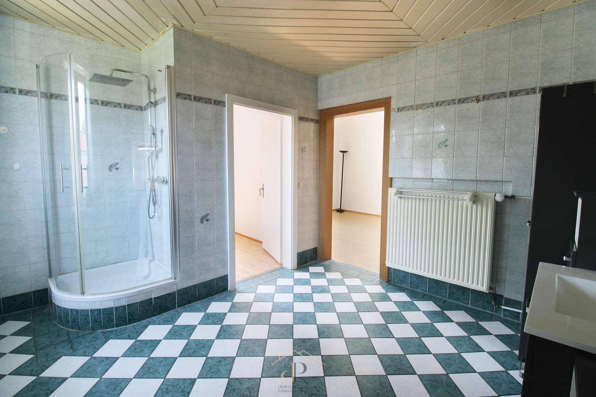 Geräumiges Badezimmer mit Duschkabine, kariertem Fliesenboden und Fenster, hell und einladend.
